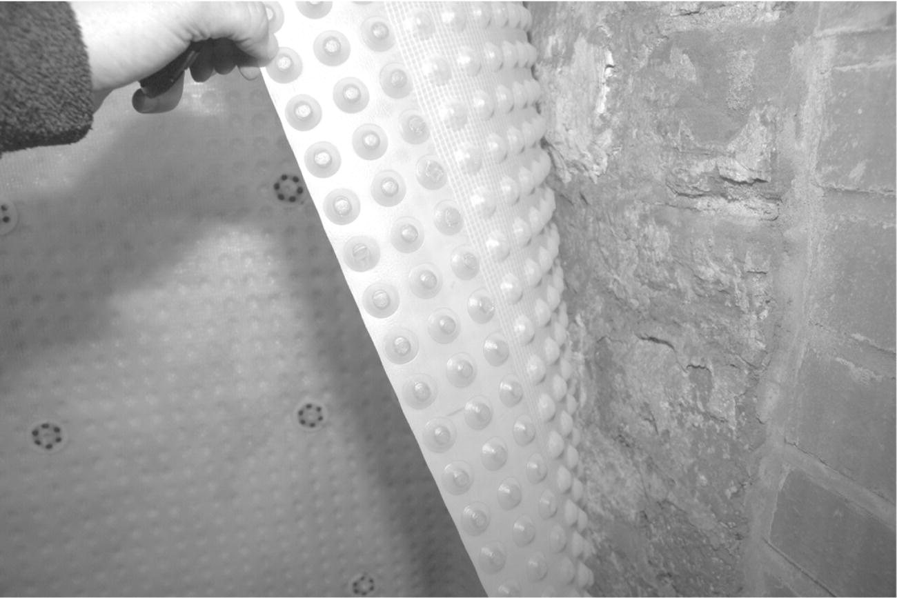 Photo of a polypropylene ventilated cavity drain sheet with a hand holding the corner of the sheet revealing the brick wall.