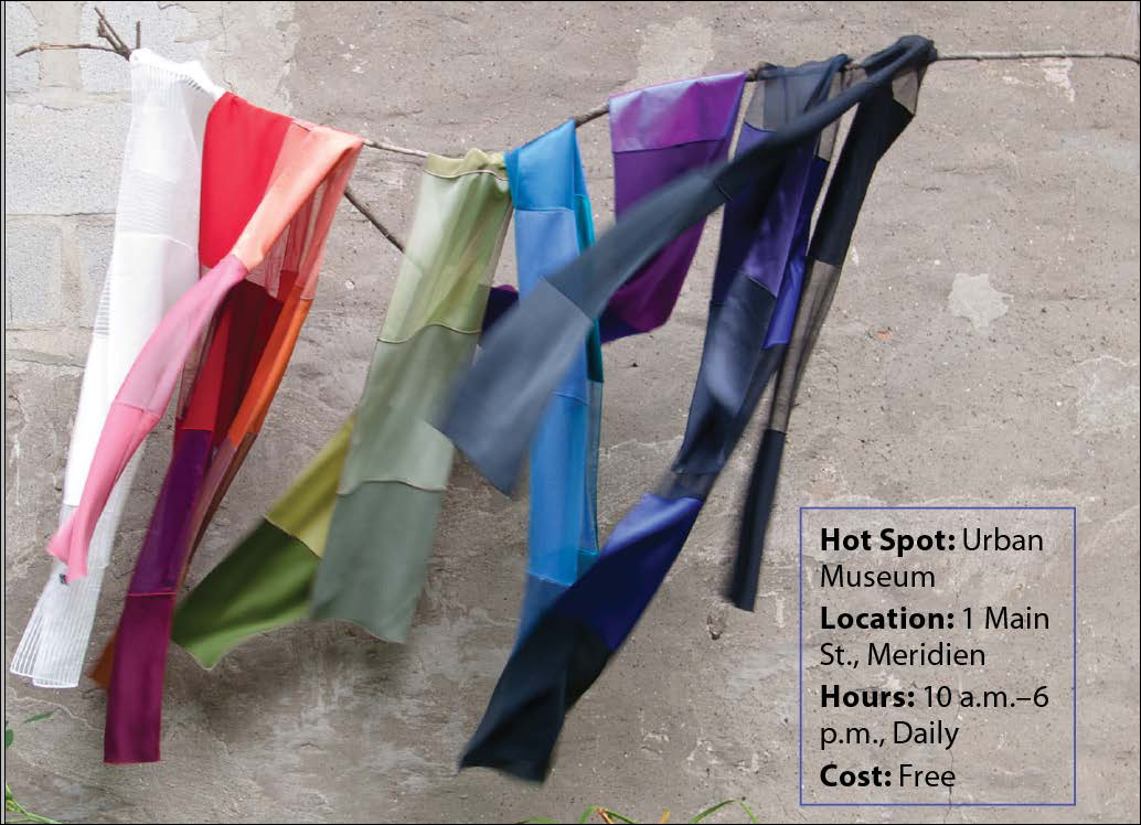 A screenshot shows a photo of some clothes hung on a thin branch of a tree. The text in the foreground reads as follows: ? Hot Spot: Urban Museum ? Location: 1 Main St. Meridien ? Hours: 10 a.m. to 6 p.m. Daily ? Cost Free