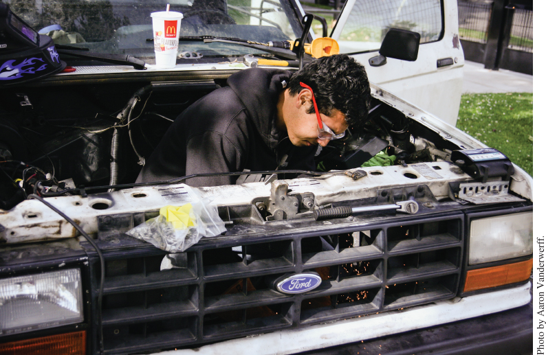 Photo displaying a man working inside a truck’s engine compartment.