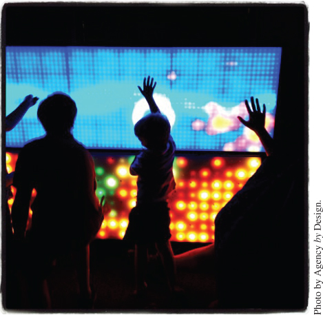 Photo displaying young visitors to the 2014 World Maker Faire engage with an interactive LED exhibit at the New York Hall of Science.
