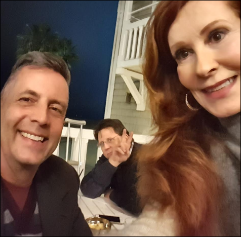 Screen capture of a selfie photo taken by Marsha Collier featuring her with a man at the left and her husband in the background showing two fingers. 