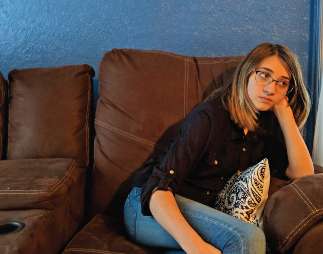 Photograph of a girl seated on a sofa, looking very quiet and sad.