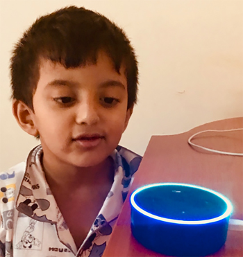 Photograph of a little boy with a Amazon Echo device placed in front of him on a table.