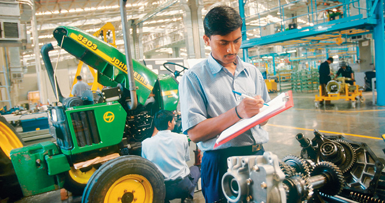 Photograph shows a factory worker taking notes about an engine on his notepad.