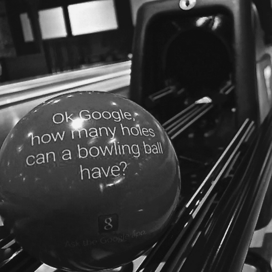 Figure representing an ad campaign to introduce Google's new voice-activation mobile search, where on a bowling ball is written, “OK Google, how many holes can a bowling ball have?” Below it is written, “Ask the Google App.”