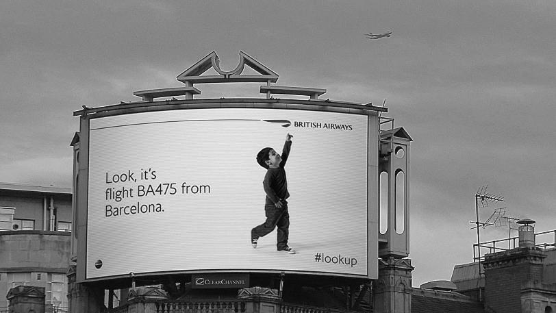 Figure depicting British Airways billboard ad where a small kid is pointing upward and on the left is written “Look, it's flight BA475 from Barcelona.” This digital billboard tracked overhead flights of British Airways, identifying in real time both flight number and destination.