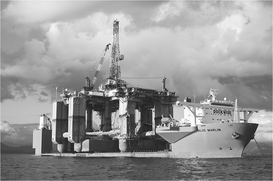 A heavy ship transports a drilling platform.