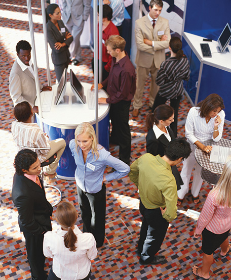 A photo shows several people huddled as groups in kiosks at a trade show.