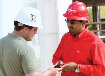 A photo shows Alim Hirani showing a product to an casually dressed man. Both of them wear a hard hat.