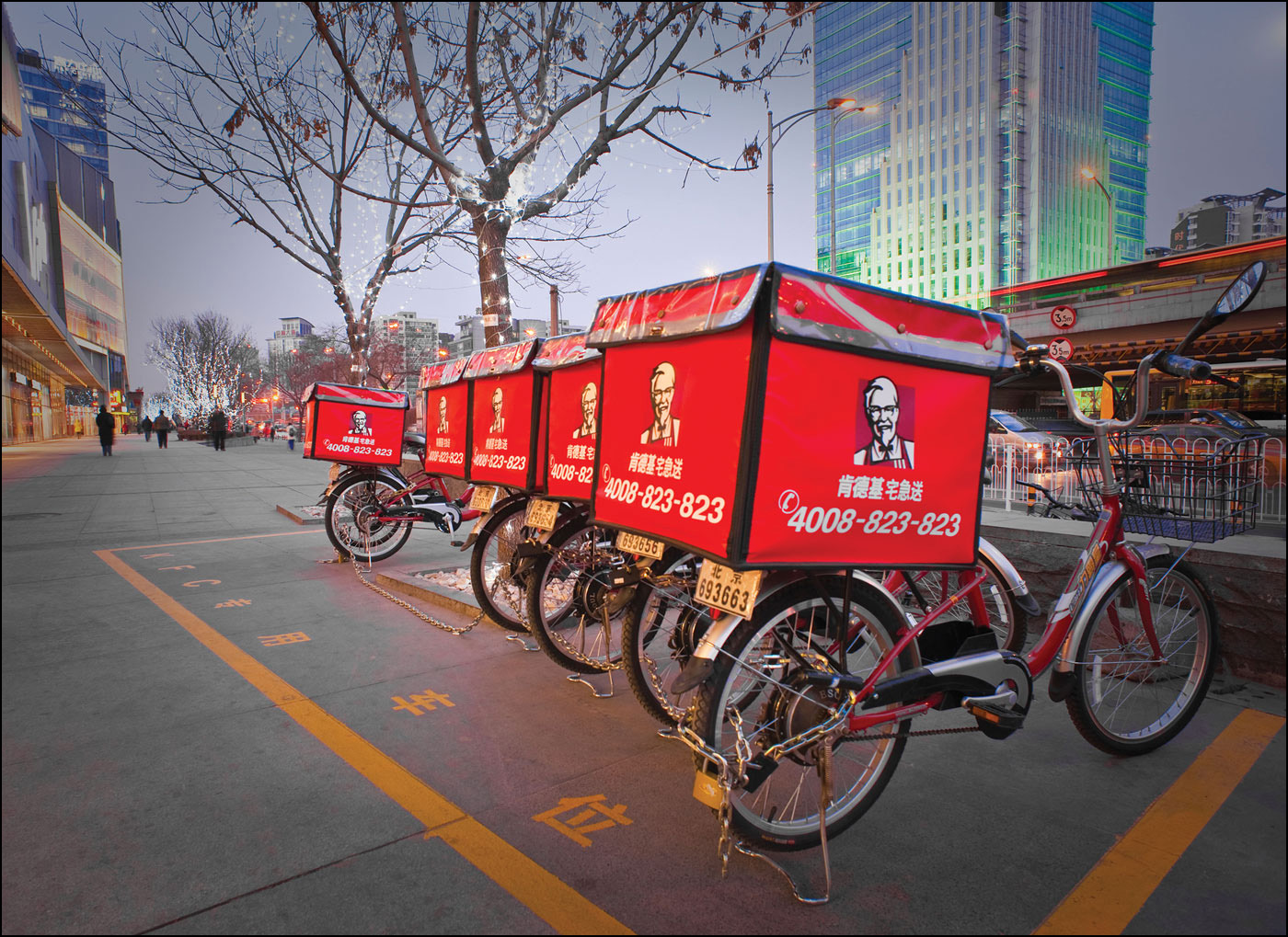 A photo shows a row of parked bikes with KFC delivery boxes attached. The text on the boxes is in Japanese language.