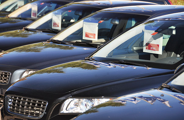 Photo shows cars lined up for sale. Price cards dangle from the rear-view mirrors.