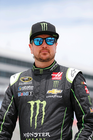 Photo shows a NASCAR driver wearing a jumpsuit covered with brand logos.