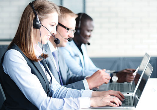 Photo shows three smiling people in business attire wearing headsets, typing on their laptops.