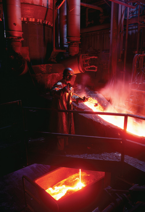 A photo of a man working in a metal and iron foundry.