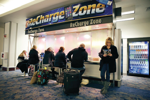 A photo of people charging their laptops and mobile phones in a Recharge Zone location.