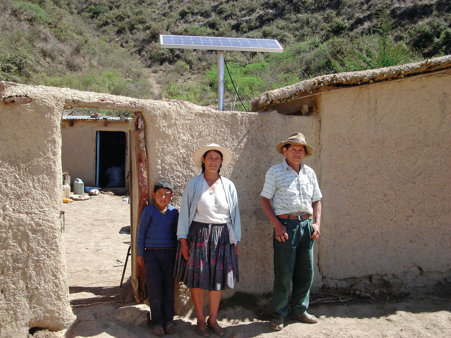 A man and a woman with a child standing displaying a PV module power at the background used as a solar home system in Bolivia.