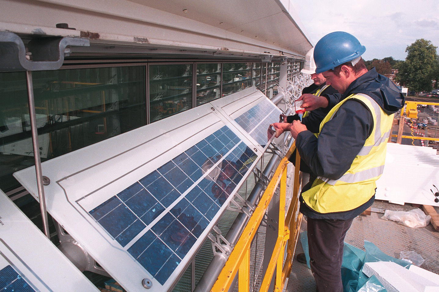 Two men replacing PV louvers with standard glass shading to provide a dual function.