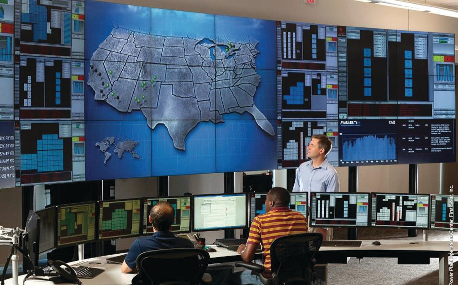 Utility‐scale PV operations center in Mesa, Arizona, USA with three men facing the tv screen with displayed US map.